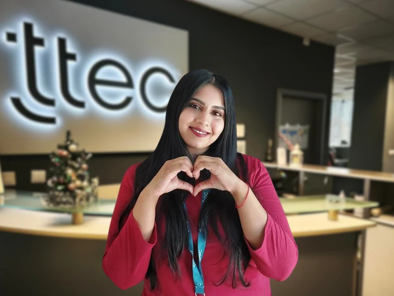 A female TTEC Mexico employee smiling and forming a heart shape with her hands.
