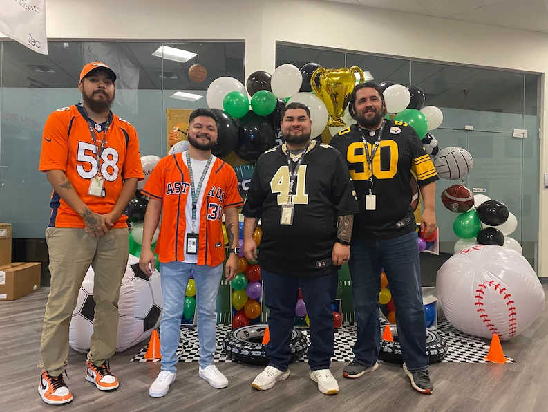 Four TTEC team members wearing different sports outfits smiling and posing together during a company event.