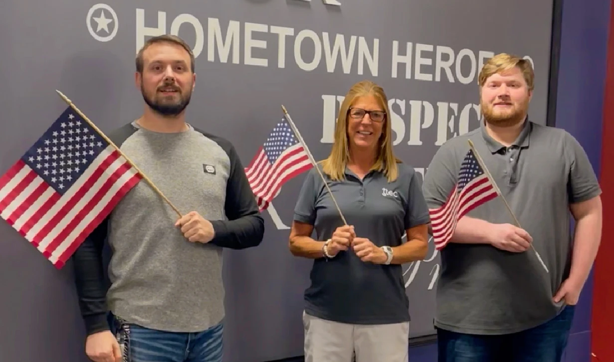 Three people holding American flags in front of Hometown Heroes mural