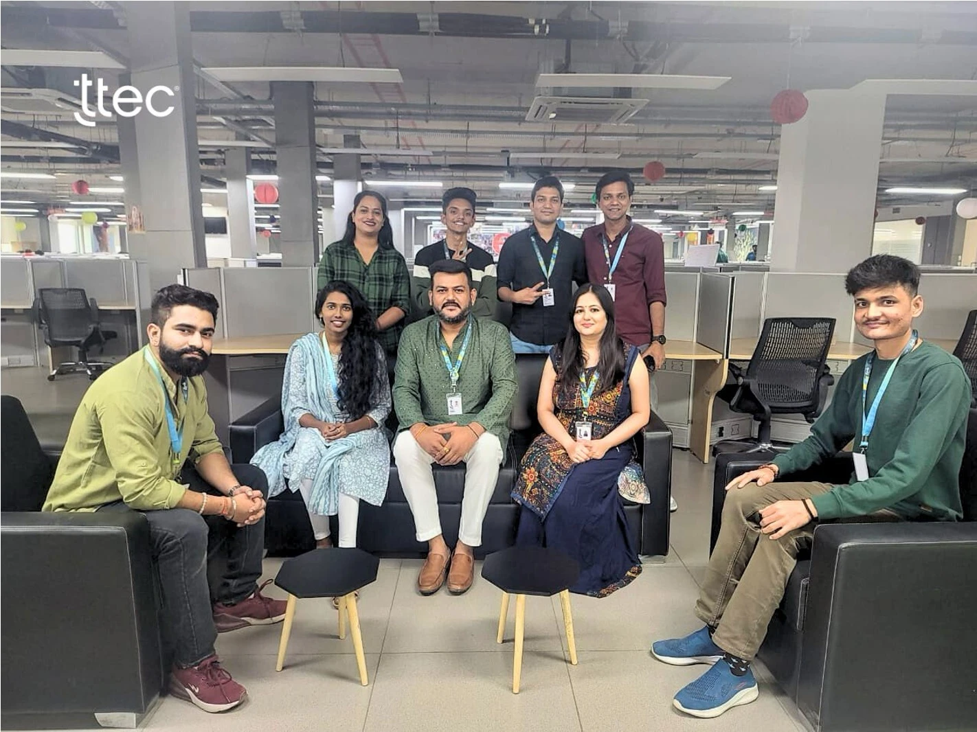 Group of nine TTEC employees in a modern office workspace.