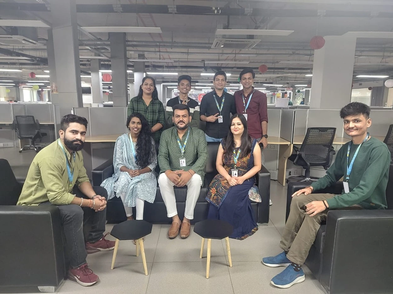 Nine TTEC employees sitting in a modern office workspace for a team photo.