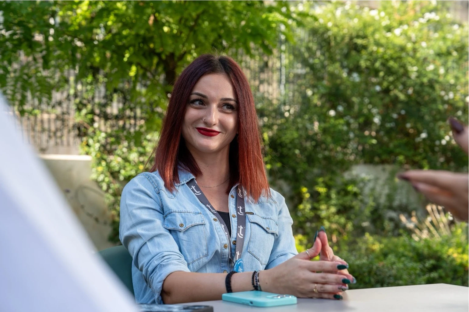 Smiling woman with reddish-brown hair wearing a TTEC lanyard and denim shirt.