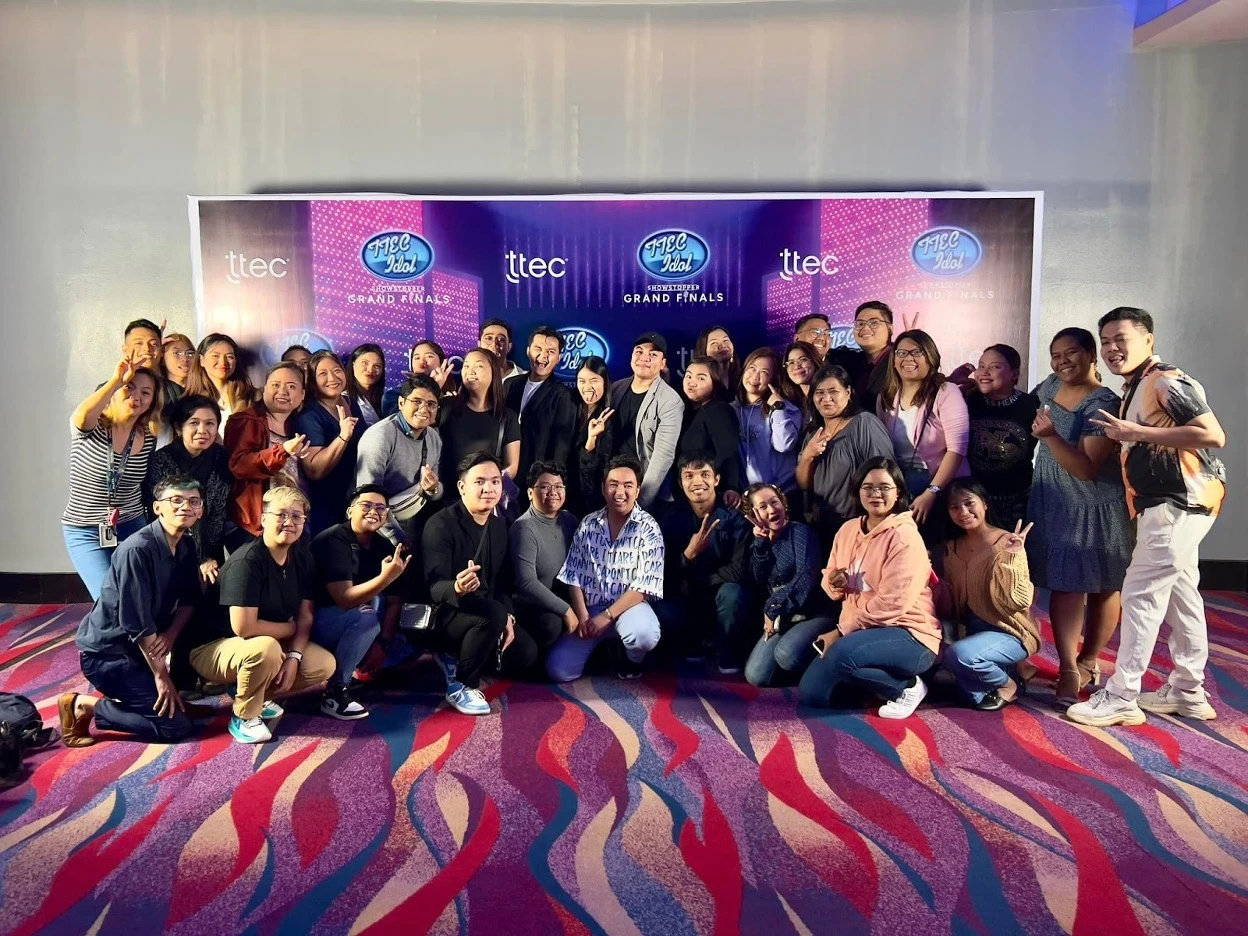 A group of TTEC employees posing in front of a ‘TTEC Idol Grand Finals’ poster.