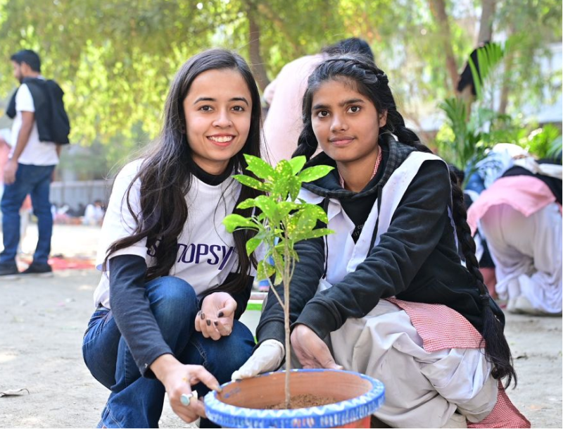 Two young girls kneeling down outside and smiling while posing with a plant.