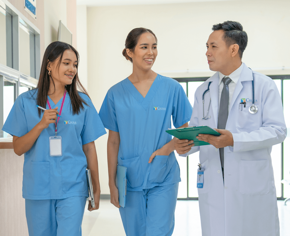 Two women in scrubs talking to a man in a lab coat