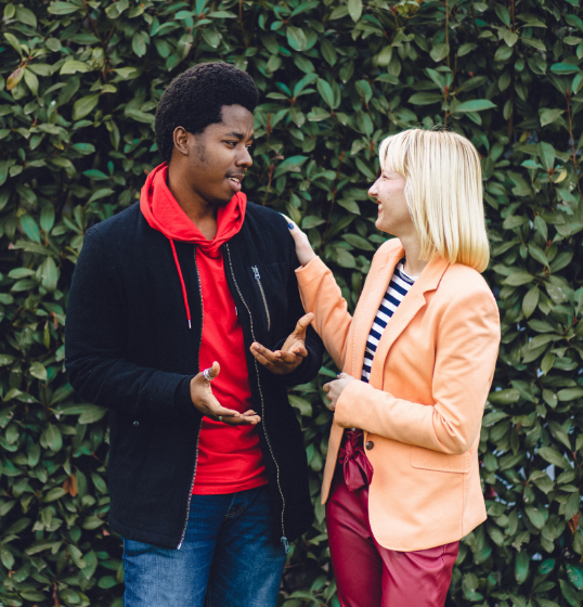 Two students speaking in front of a hedge