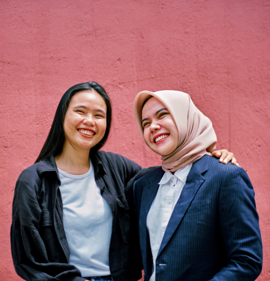 Two students smiling in front of pink wall