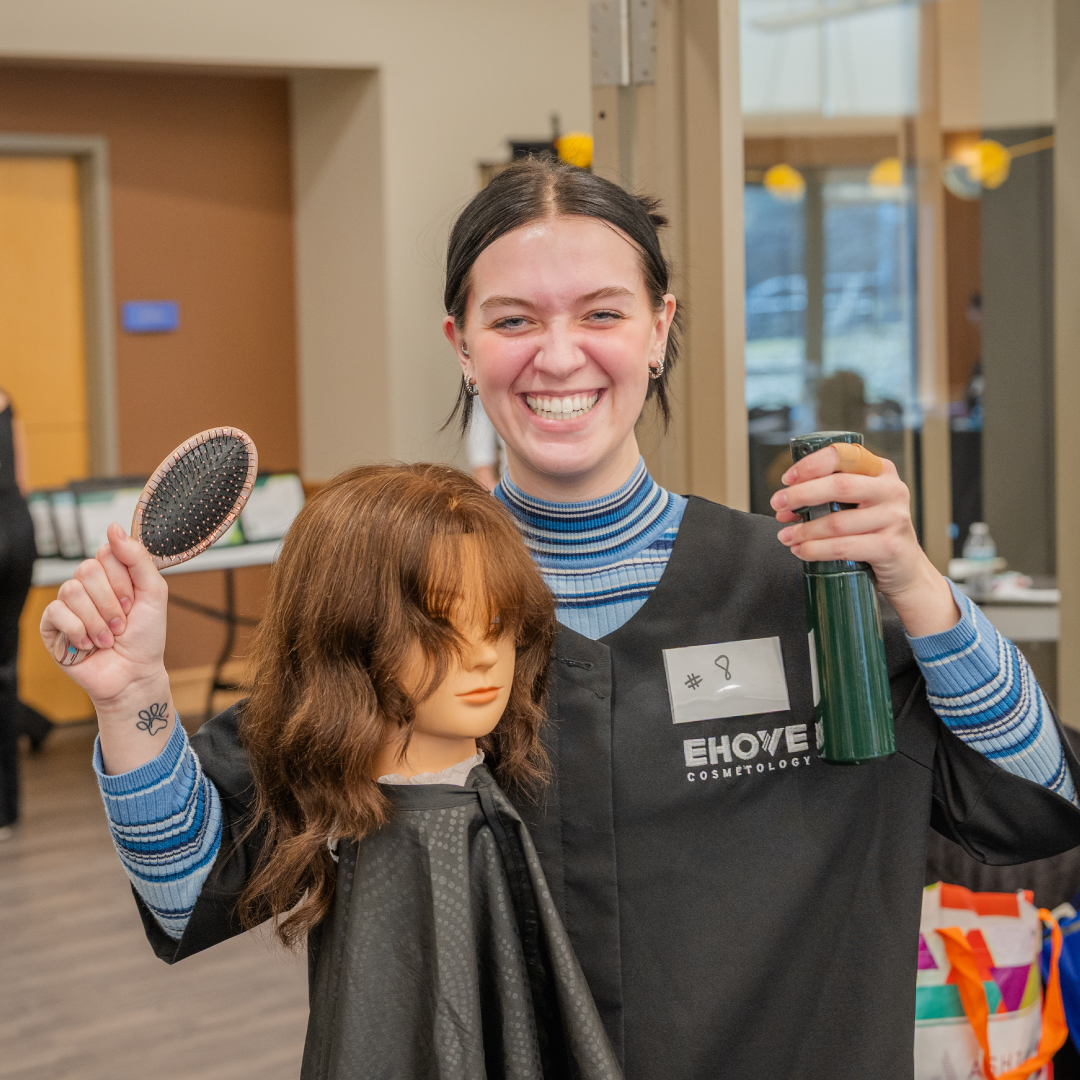 Smiling student with mannequin head, brush, and spray bottle