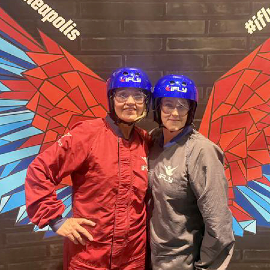 Tami and her franchisee Kim stand in front of a winged selfie backdrop at iFly, a skydiving simulation experience