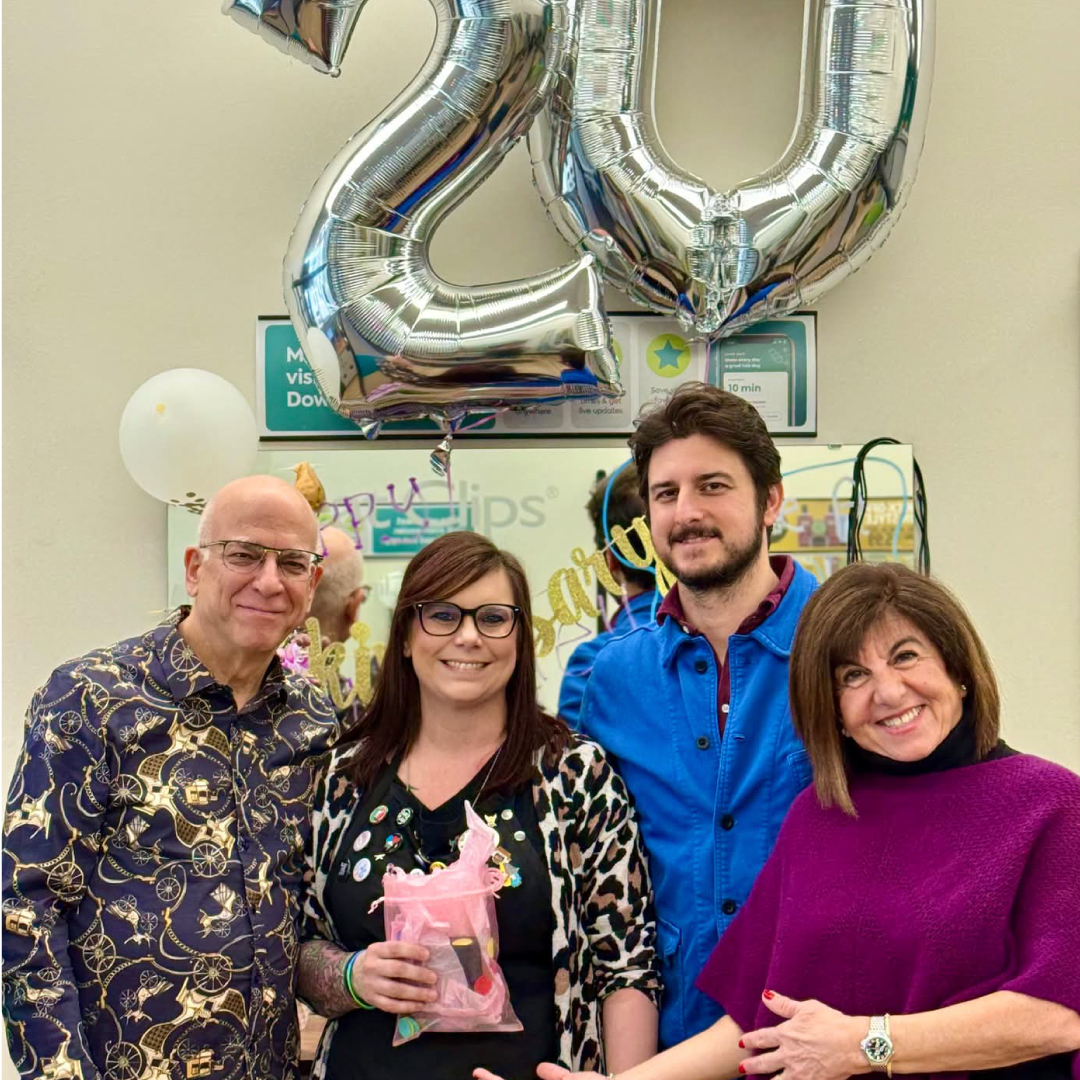 Leslie stands next to her franchisees, all smiling in front of her salon station. Balloons decorate her station to celebrate 20 years.