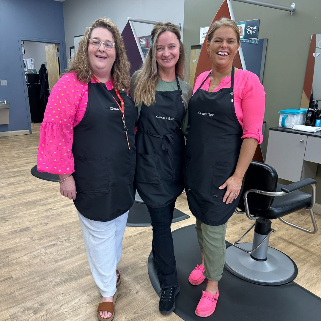 Team of three smiling stylists stand together in salon.