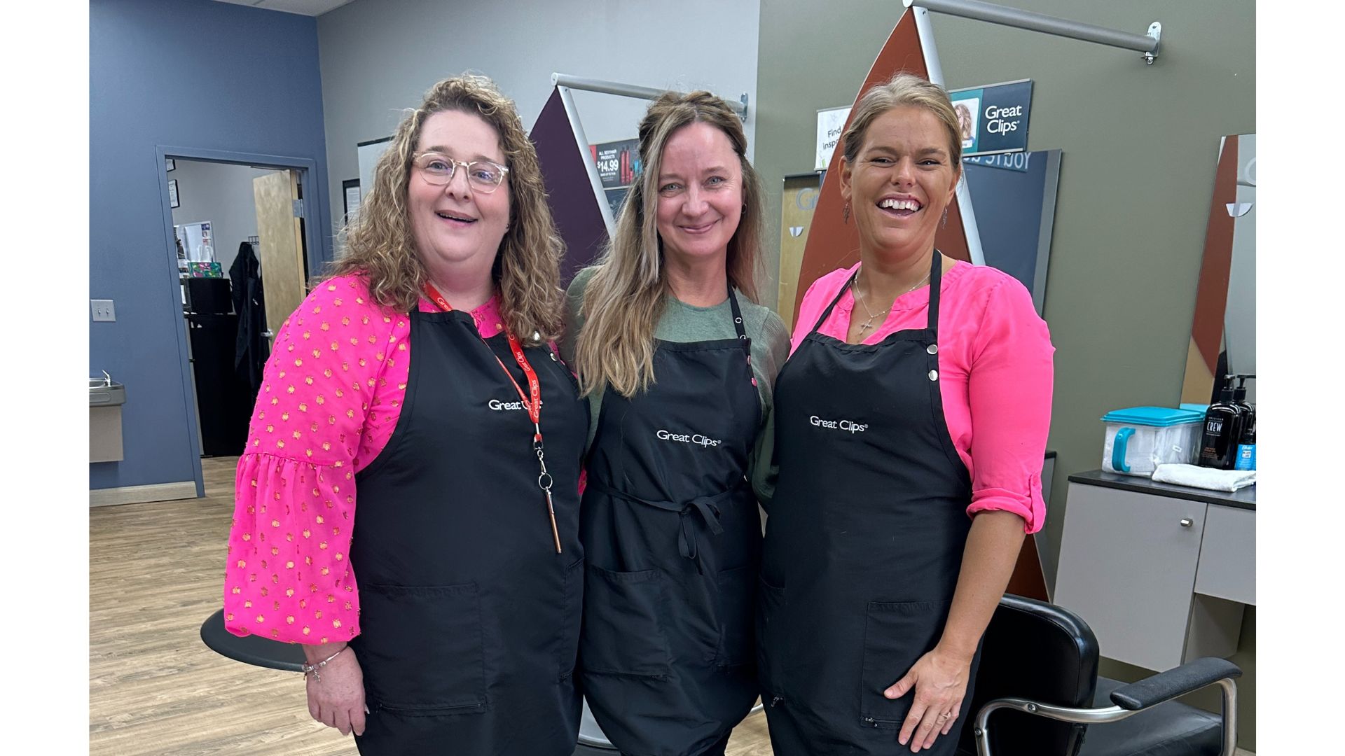 A smiling team of three stylists stands together in salon.