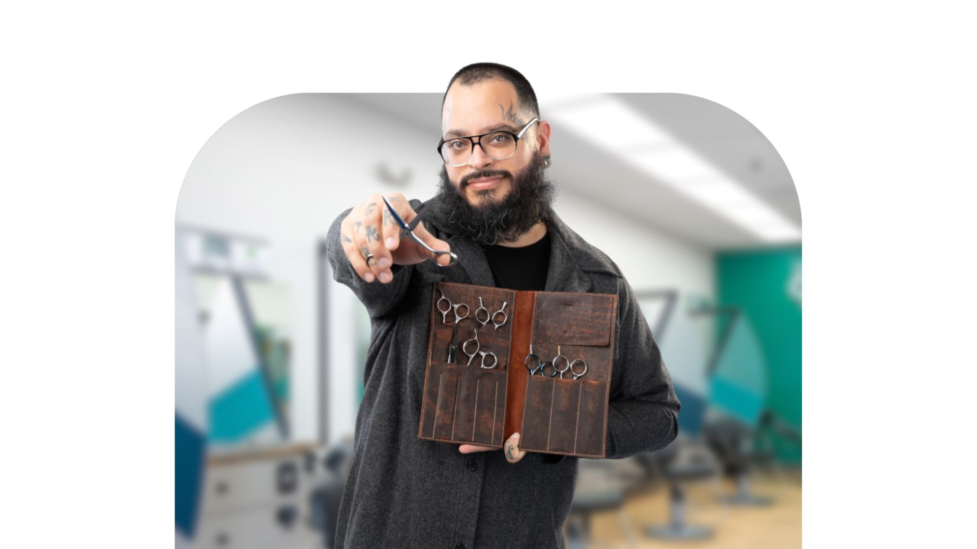 A confident barber holds his kit of cutting tools while extending his shears toward the camera.