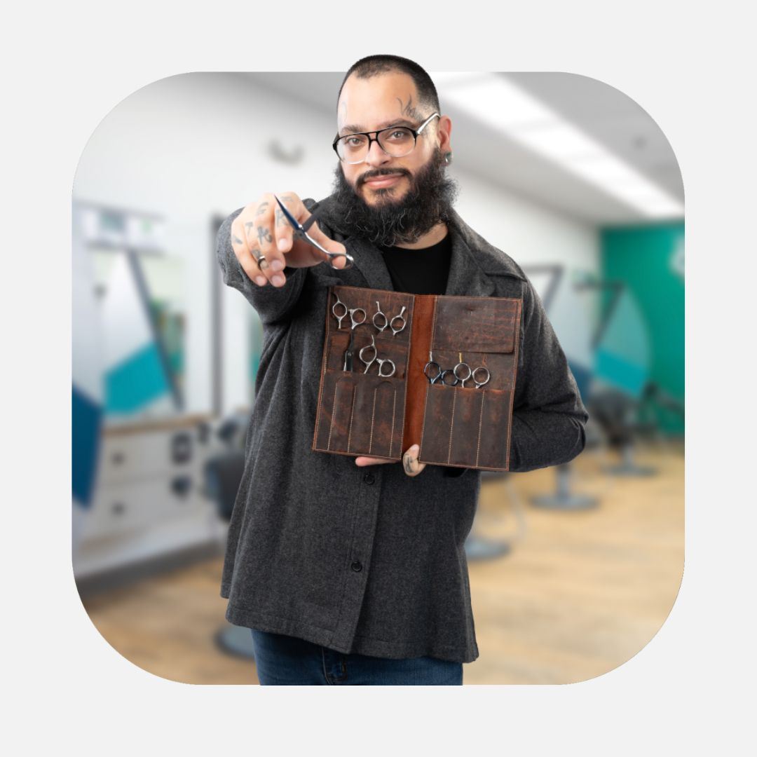 Confident barber holding his kit of cutting tools and pointing his shears toward the camera