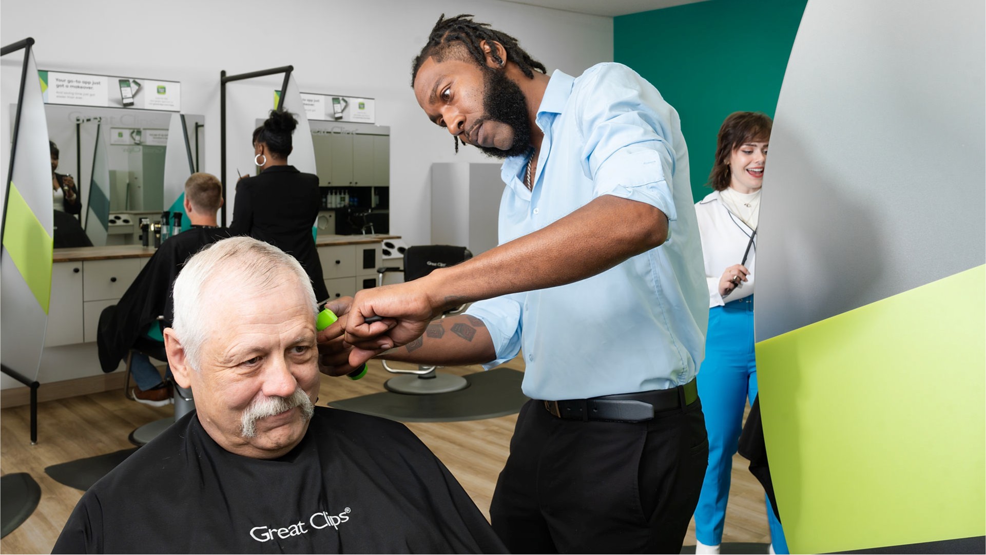 Male stylist in Great Clips salon cutting an older male customer's hair with a clipper
