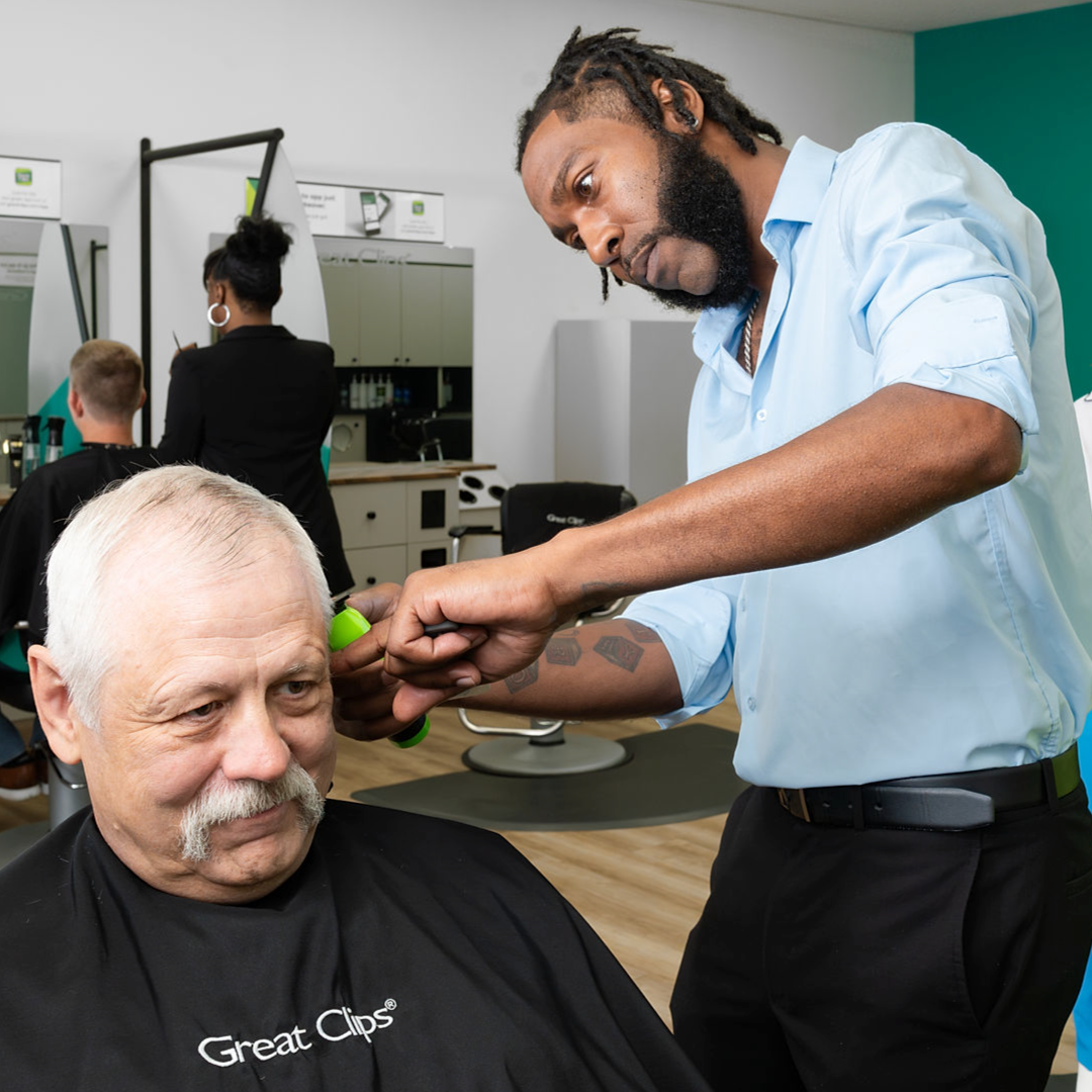 Male stylist in Great Clips salon cutting an older male customer's hair with a clipper