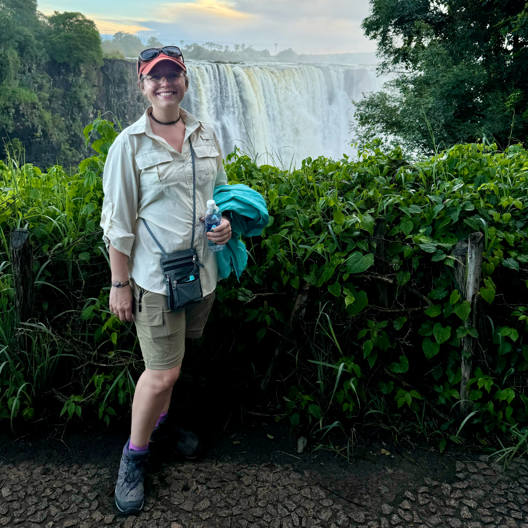 Smiling woman stands in front of large waterfall while on vacation in South Africa