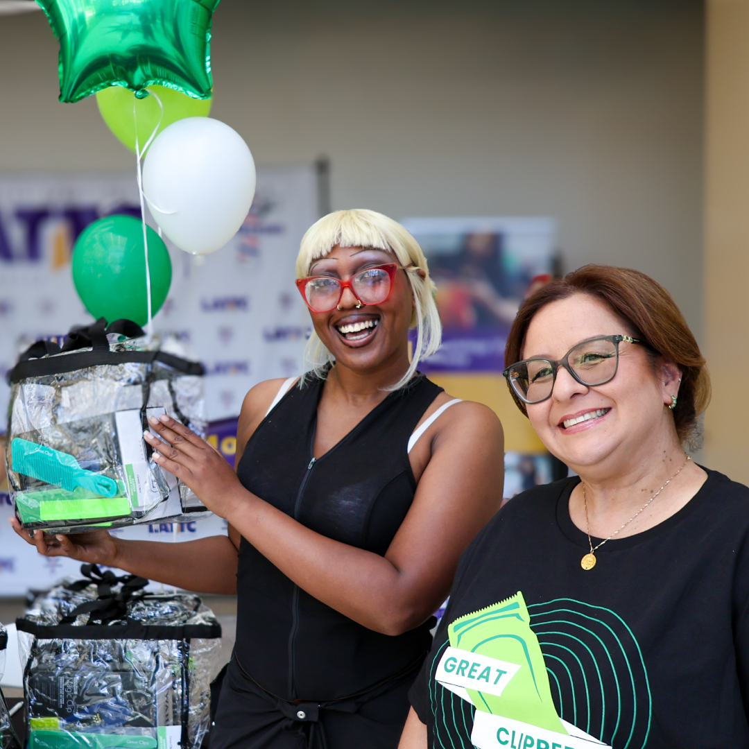 Smiling student holds clipper gift, standing next to school recruiter and a display of green balloons