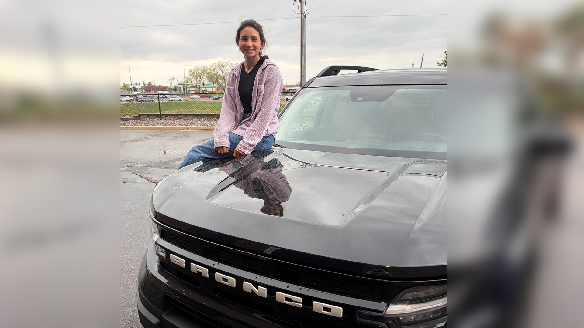 Natalia sits on the hood of her new Bronco, smiling