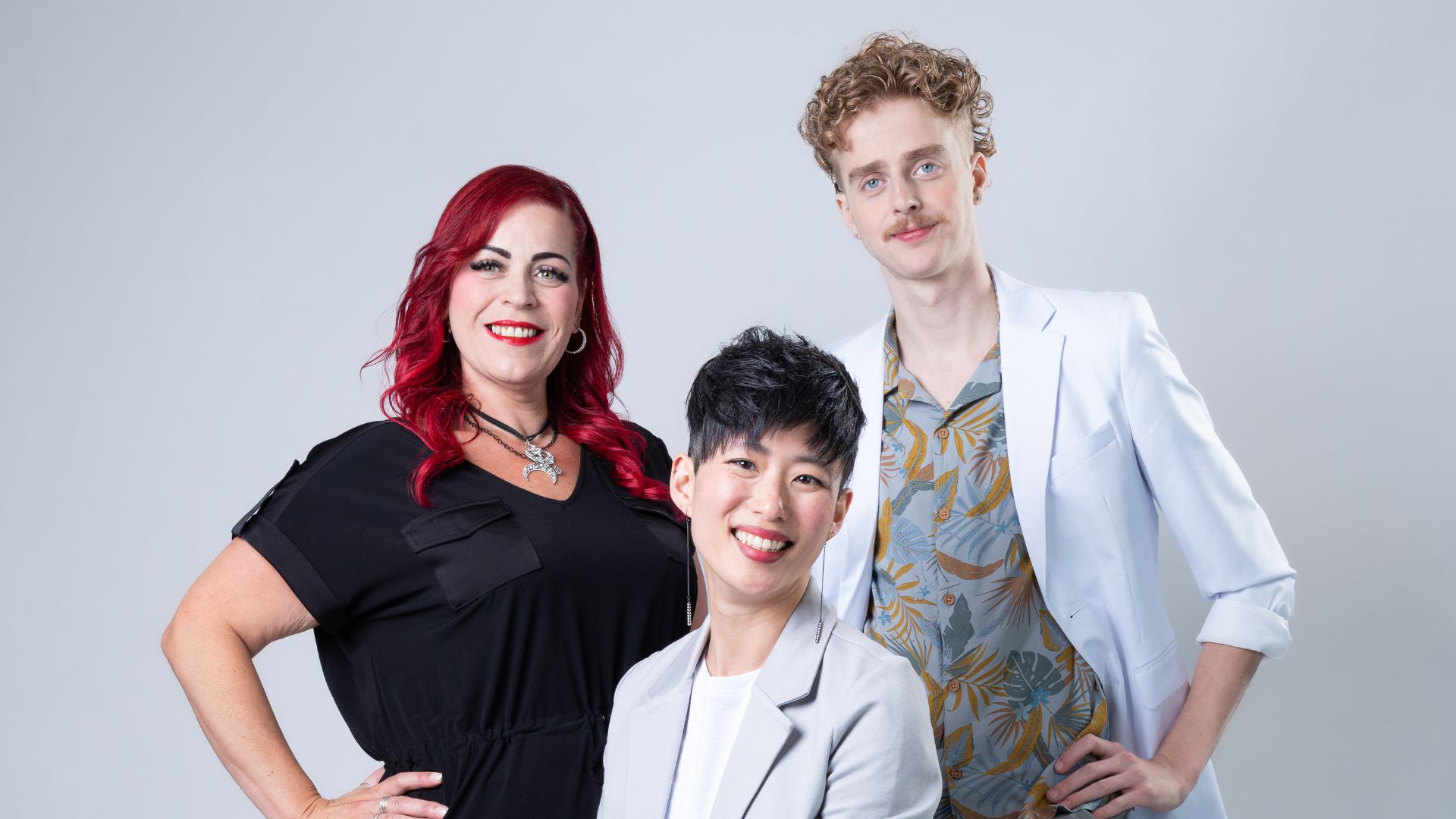 A Great Clips educator stands smiling with two models wearing different versions of new trend haircut.