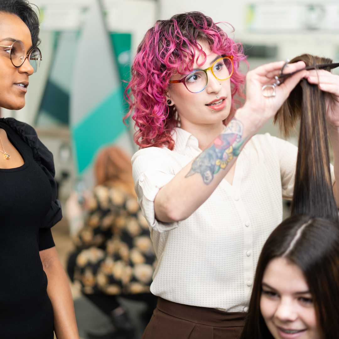 A new stylist cuts a long layered haircut while an experienced stylist observes