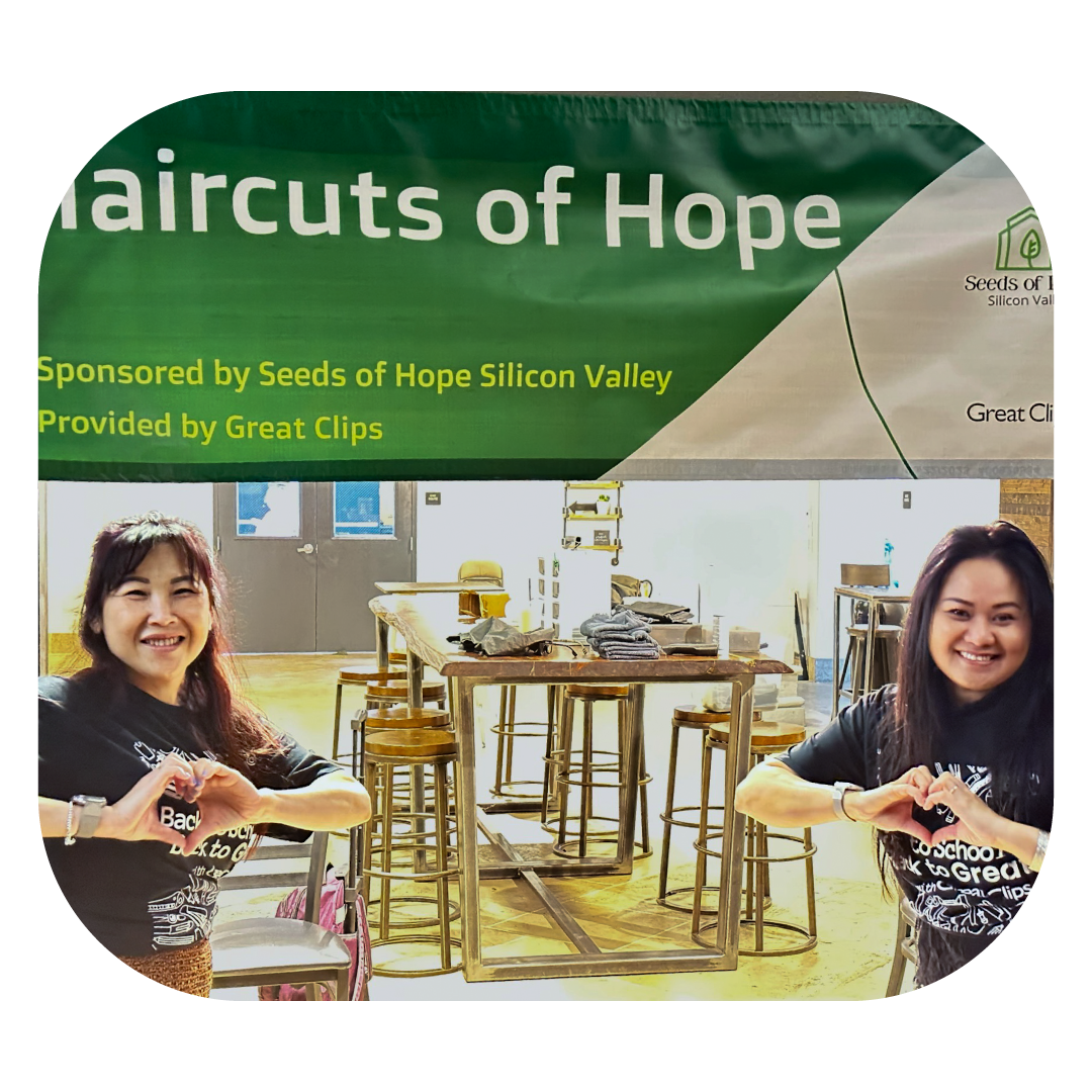 Two stylists holding their hands in heart shapes in front of a banner that says Haircuts of Hope