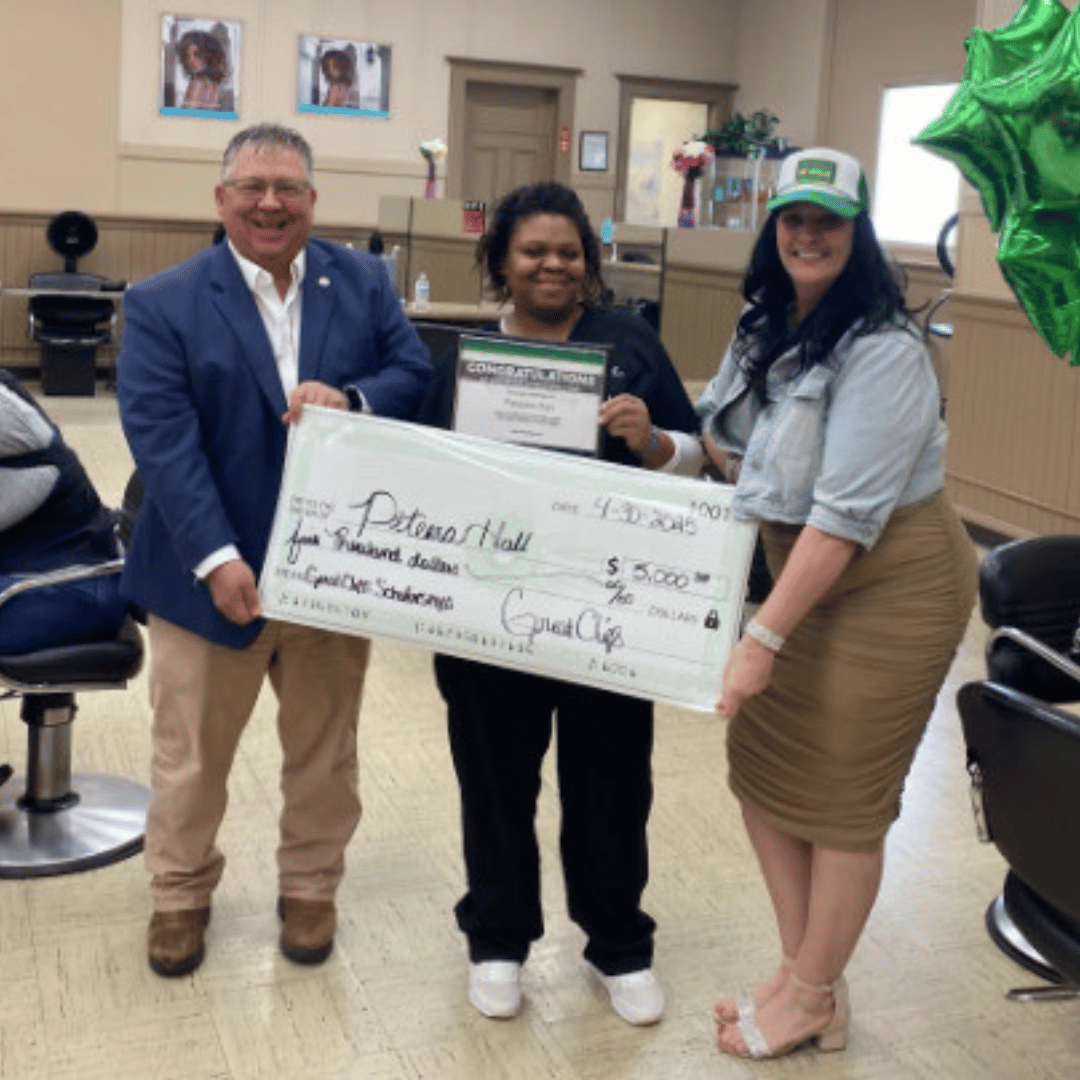 Smiling student inside cosmetology school holding large scholarship check