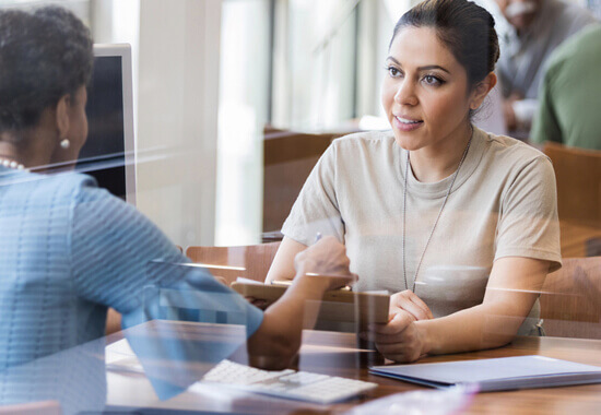 female service member in military fatigues, sitting and conversing with a woman across a desk