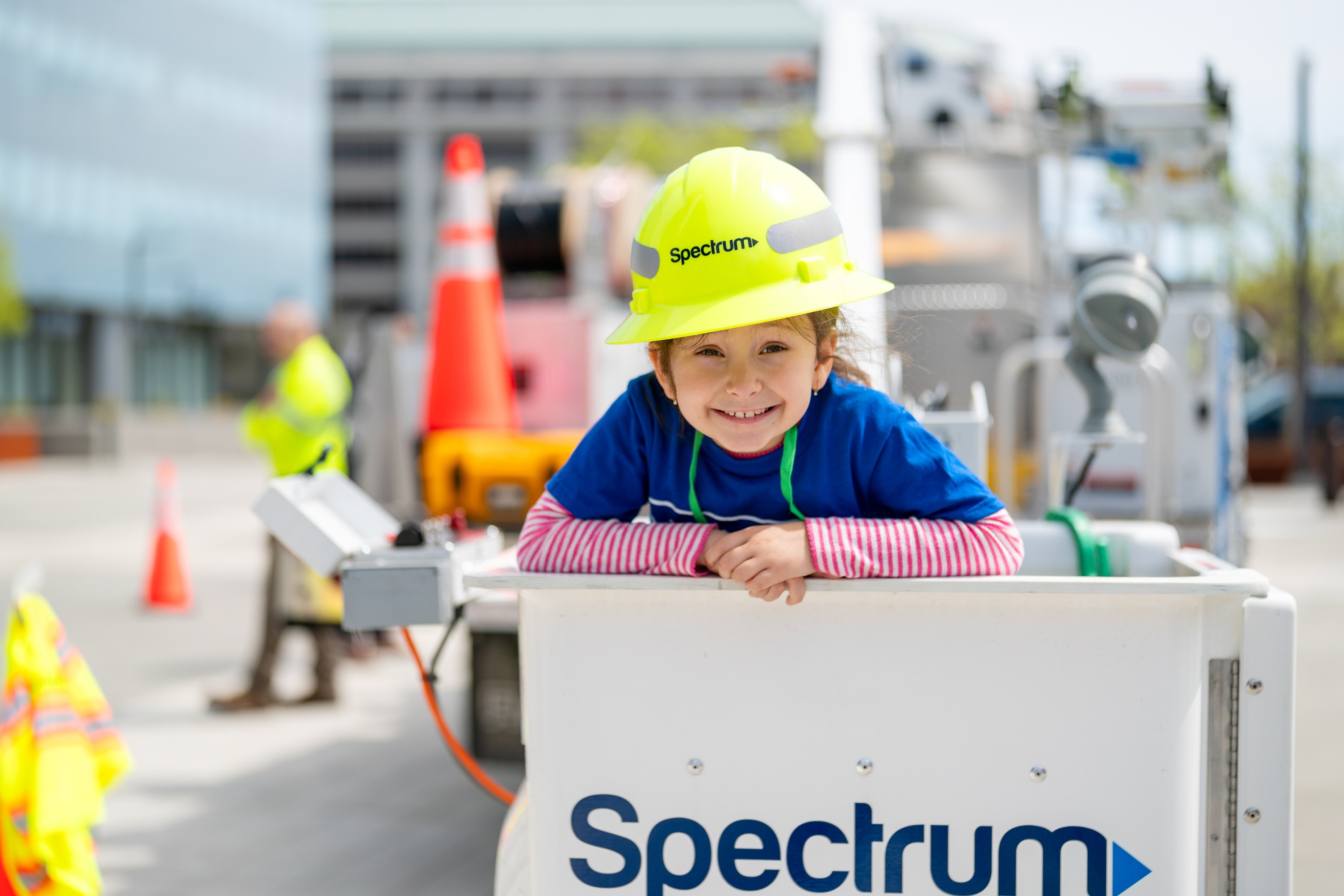 little girl in yellow hardhat smiles from a bucket in a tech truck