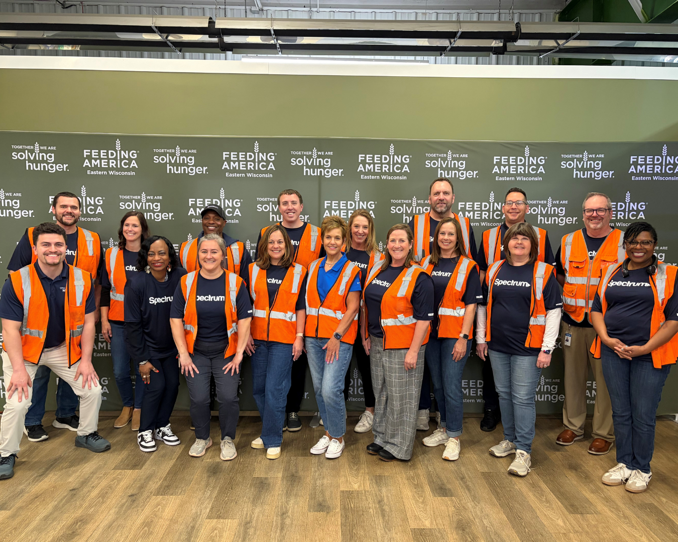 more than a dozen volunteers in orange safety vests post in front of Feeding America signage
