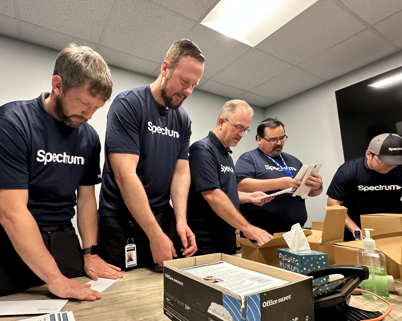 4 men in Spectrum blue t-shirts help with admin tasks in office