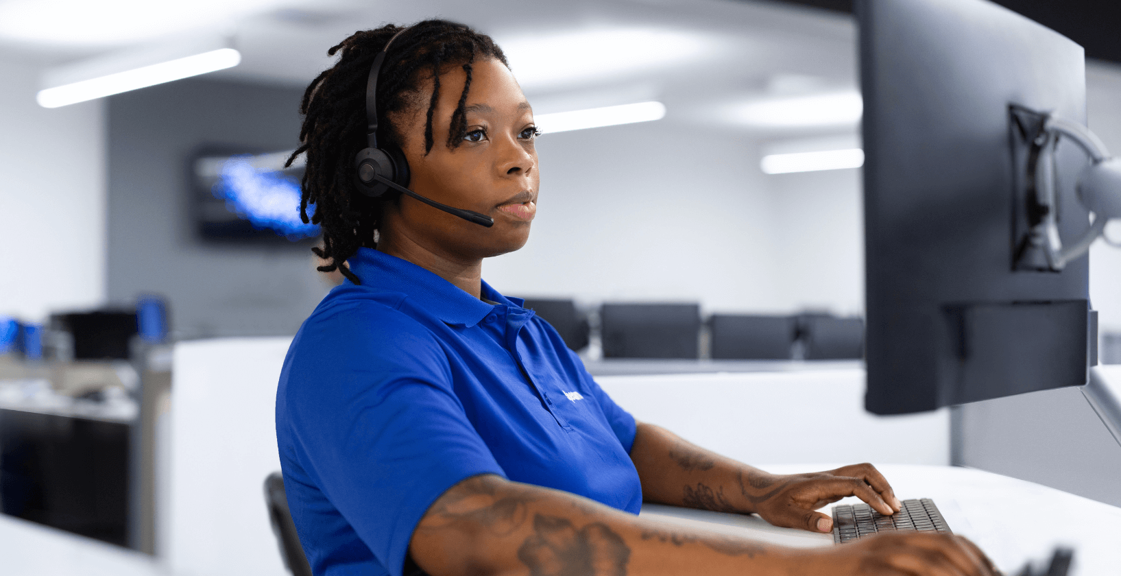Call center employee in blue polo shirt, sitting in front of a computer and wearing a headset