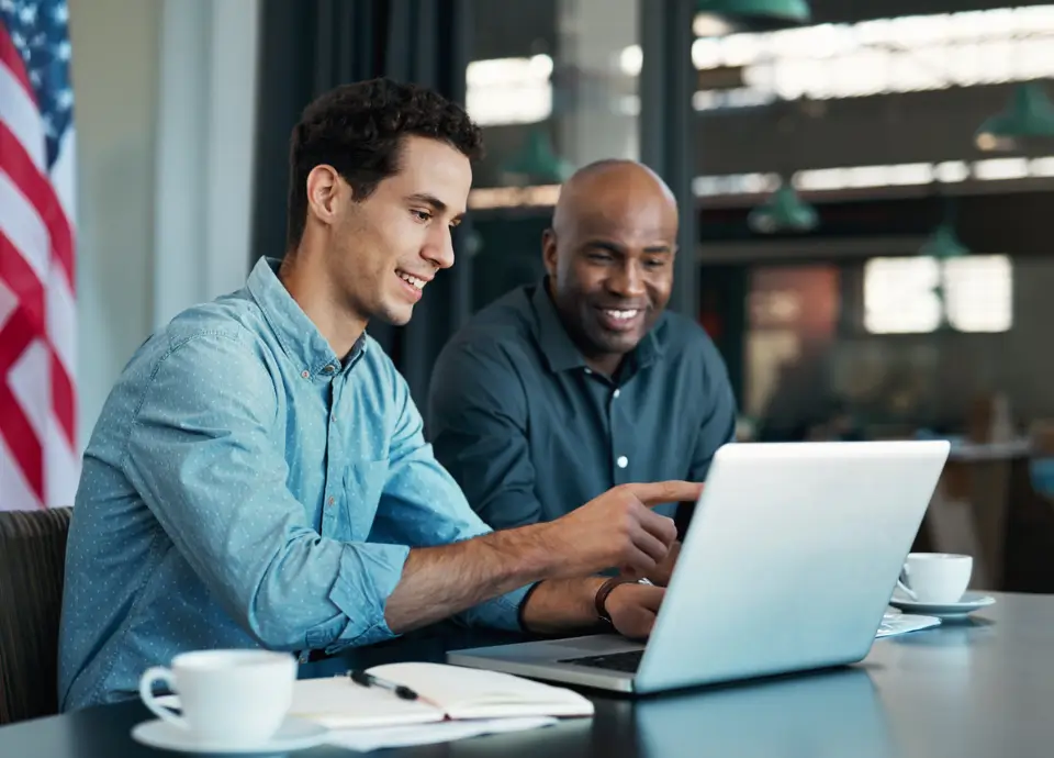 two individuals speaking with each other in front of a laptop with an american flag in the background