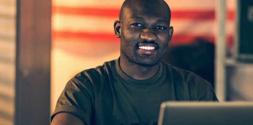 male service member sitting behind a laptop and smiling
