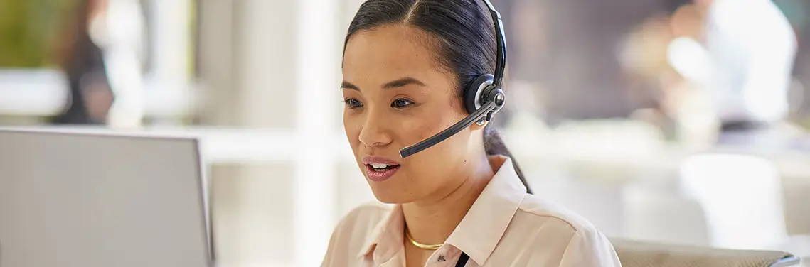 woman talking on the phone wearing a headset and working on her computer