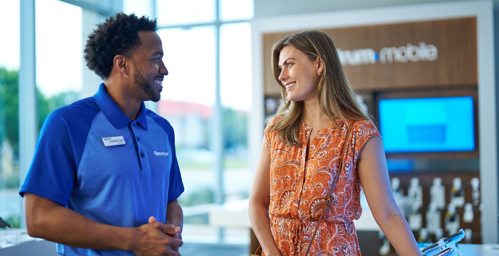 black male retail employee wearing a blue polo shirt, chatting with a female customer inside a store