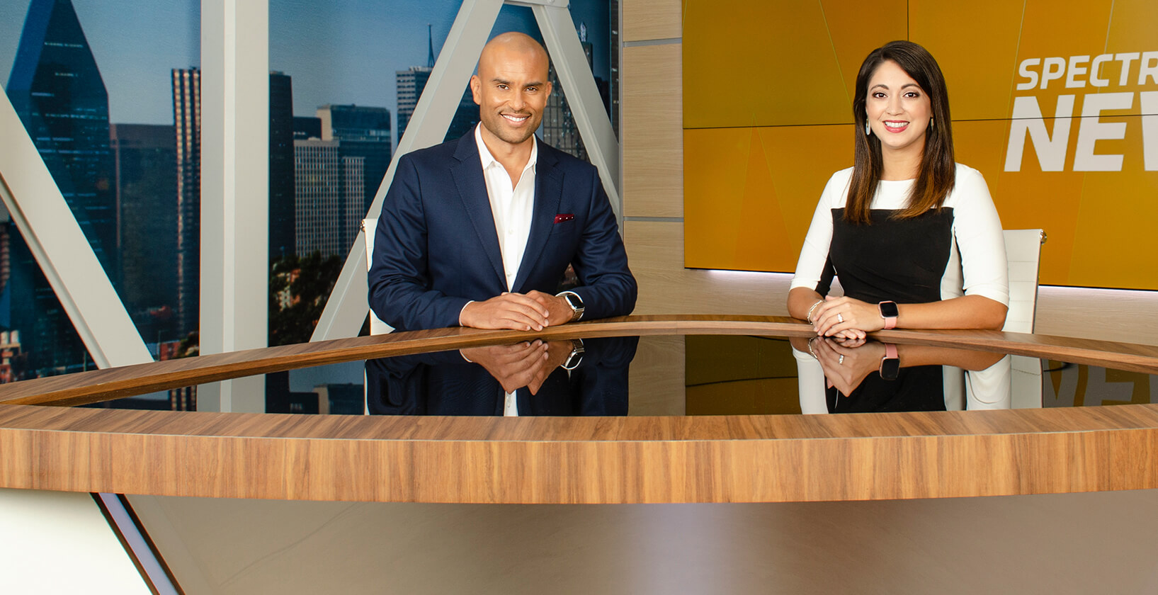 male and female co-hosts seated at a desk on the set of a Spectrum News television program