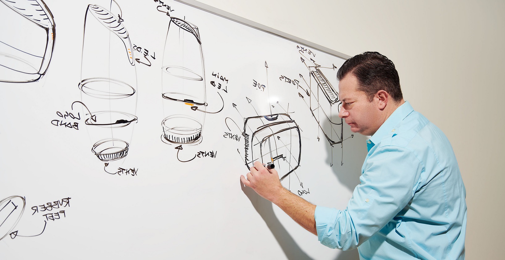 middle-aged man drawing technical designs on a whiteboard