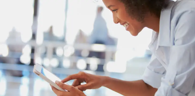 female wearing a white collared shirt holding an iPad and smiling at the device