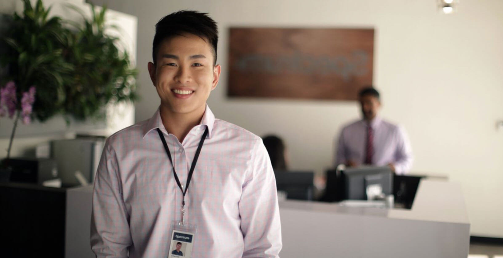 smiling young asian male intern in office attire, wearing a lanyard with an ID card attached around his neck