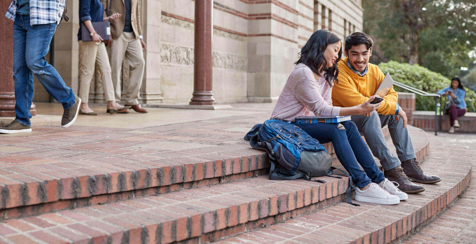 male and female college student sitting outside a building on campus, chatting