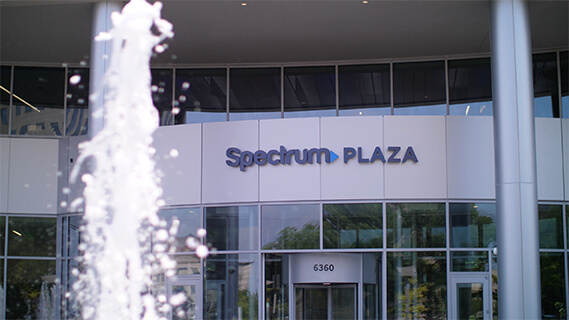 Image of exterior front entrance of Spectrum Plaza building showing a water fountain feature and contemporary architecture