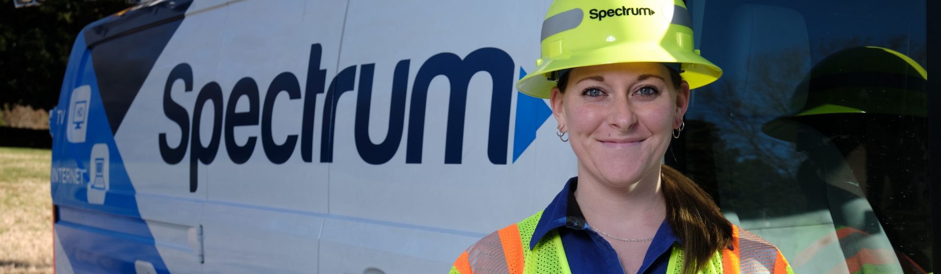 Female employee with hardhat is smiling while standing next to a Spectrum van