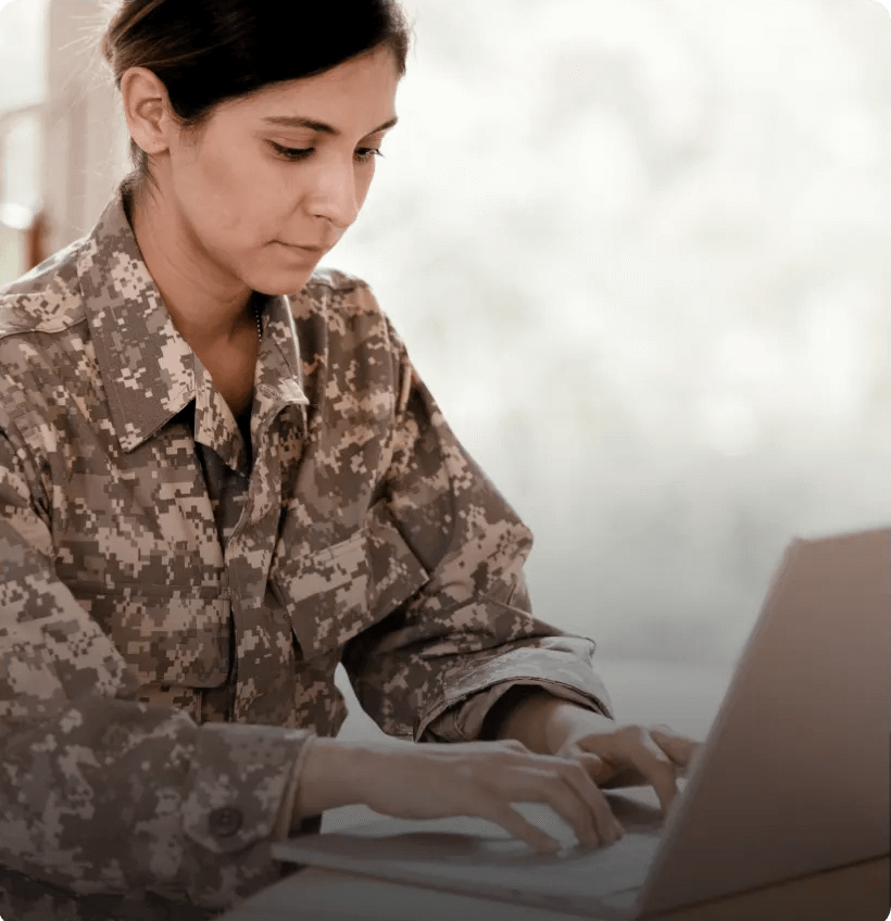 A woman in military fatigues typing on a laptop.