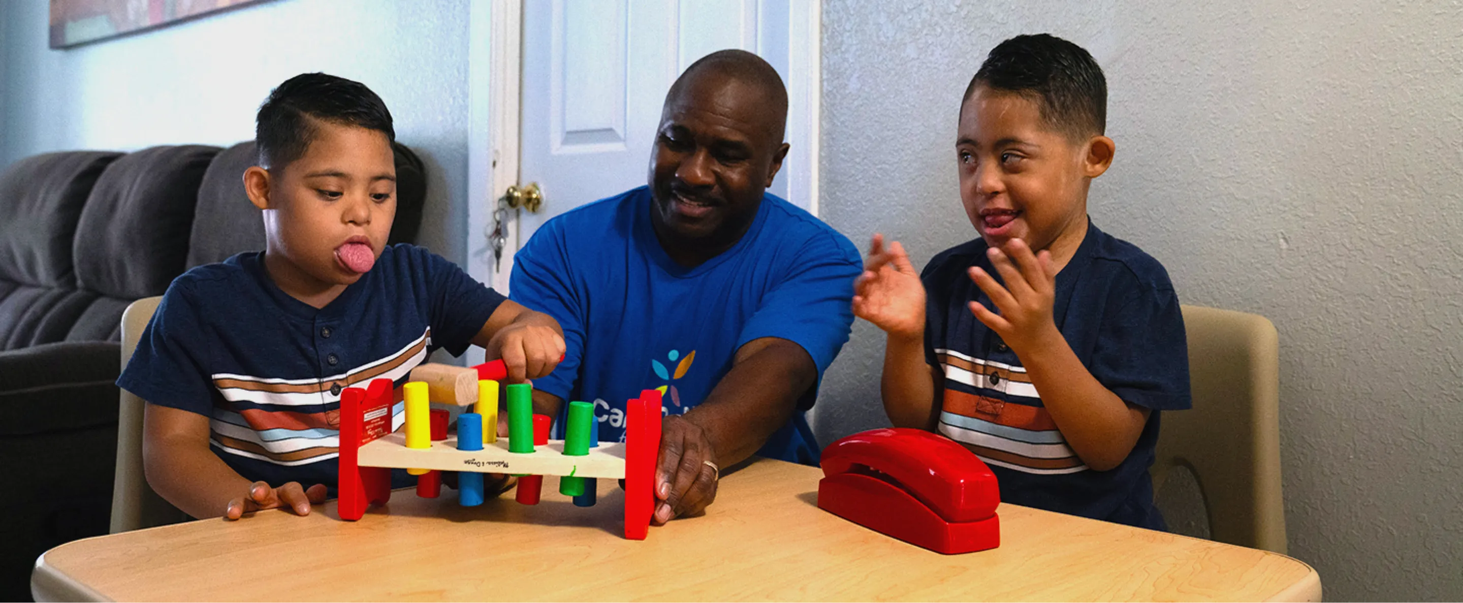 A COFK nurse sits at a table, engaging in play therapy with two children