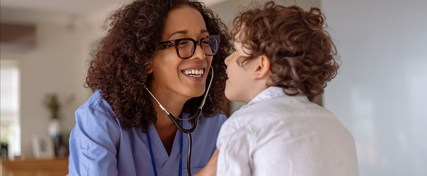 A nurse curly hair wearing a blue top and a stehescop sits in front of a patient.