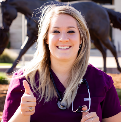 Veterinarian smiling and giving a thumbs-up while wearing scrubs and a stethoscope.
