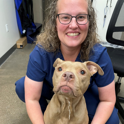 Veterinarian smiling with a tan dog in a veterinary hospital exam room.