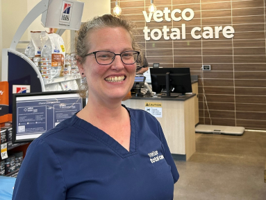 Veterinarian smiling with a tan dog in a veterinary hospital exam room.