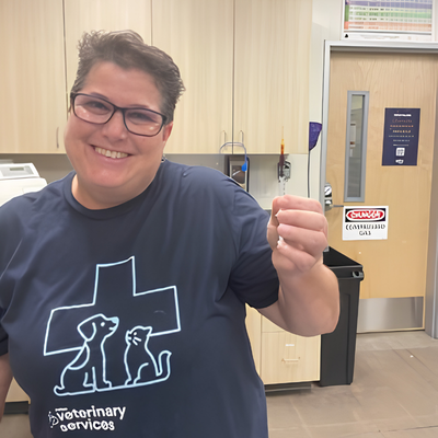 Smiling veterinary team member holding a syringe in a veterinary hospital exam room.